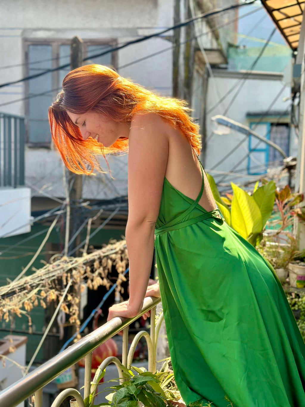 Woman in a green dress standing on a balcony with buildings and plants in the background