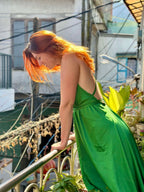 Woman in a green dress standing on a balcony with buildings and plants in the background